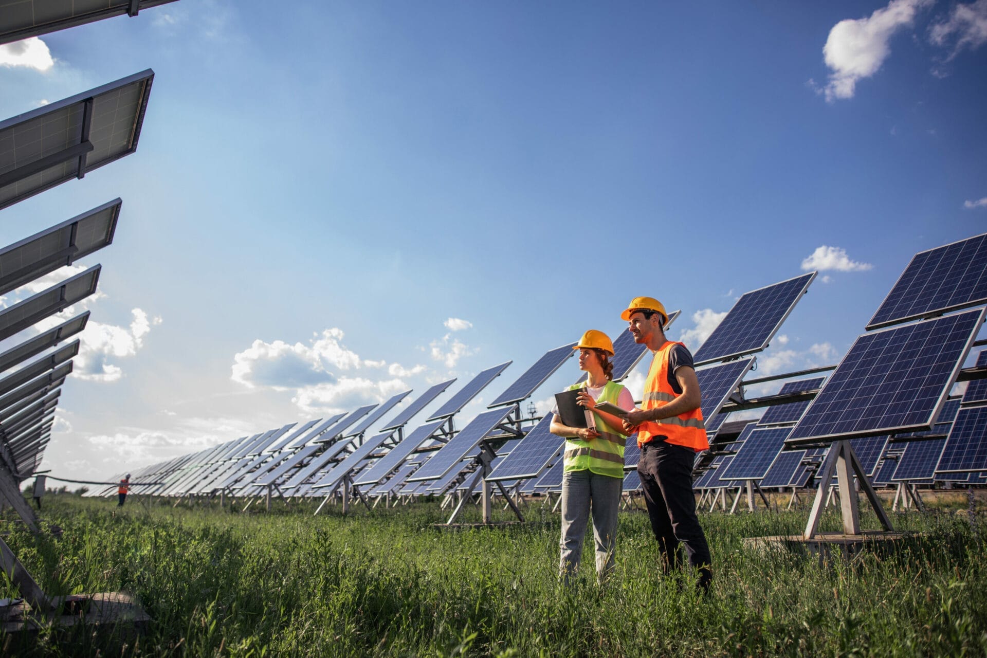 Portrait of engineers spending time outside near solar panels. Two workers: woman and man in special uniform pointing at something and smiling